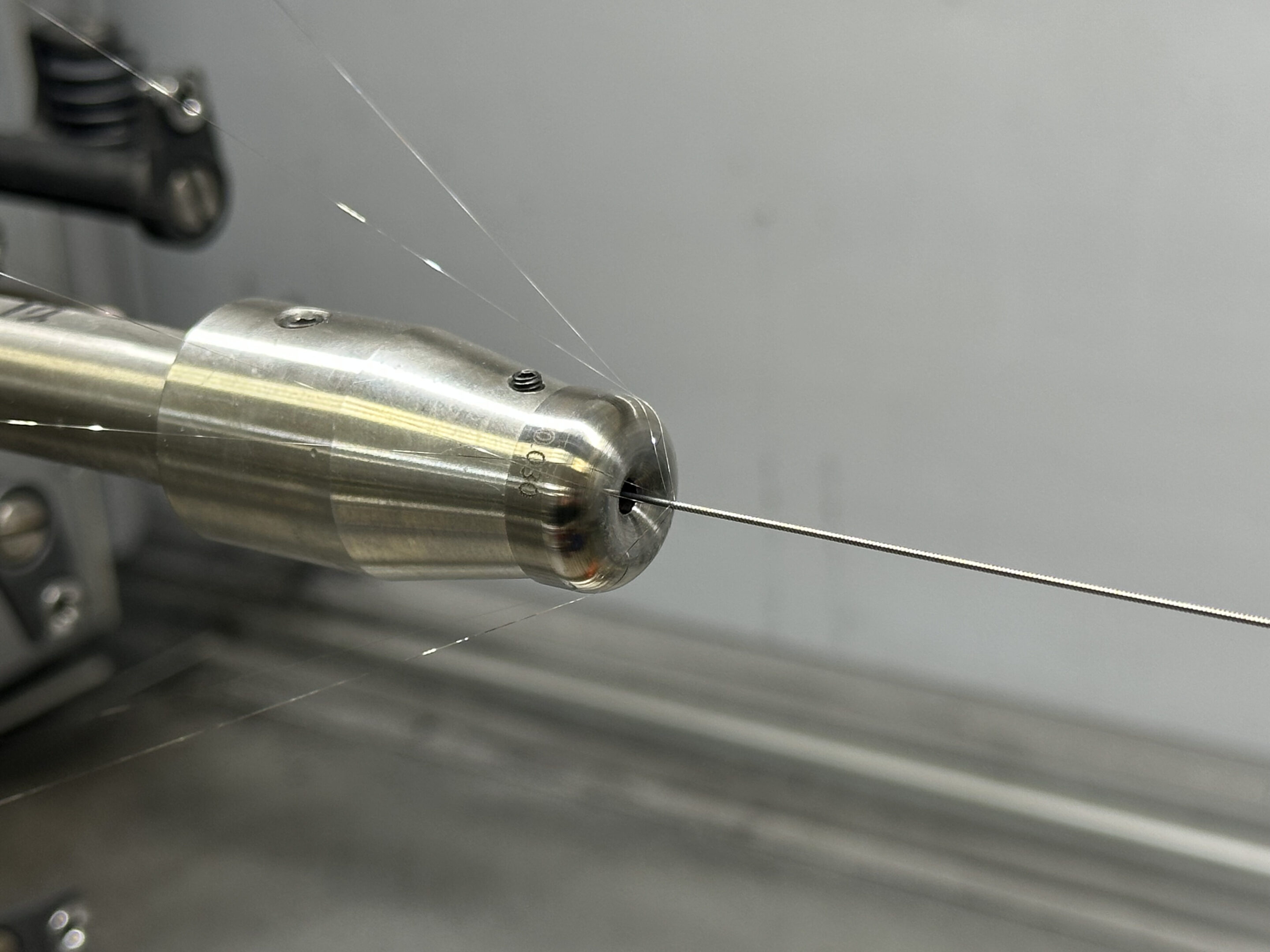 Close-up of a metal nozzle with a thin wire or filament.
