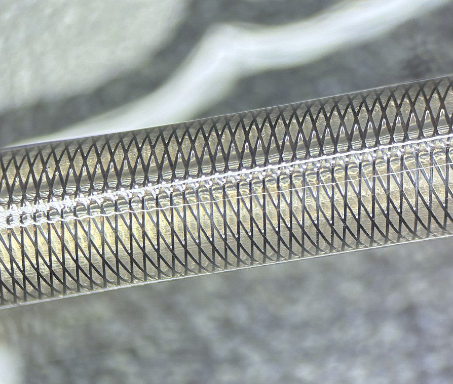Close-up of a coiled metal spring with a fine wire mesh wrapped around it.